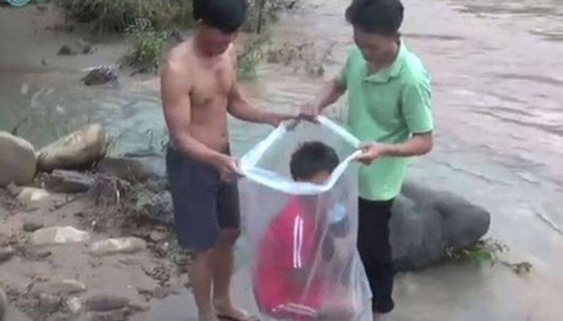 Children travel in plastic bags across flooded river so they can go to school