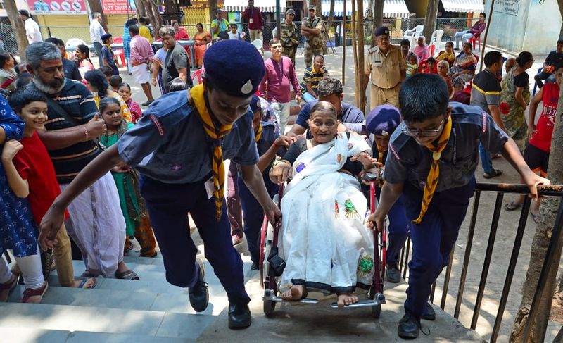 ನಡೆಯಲಾಗದ ವೃದ್ಧೆಗೆ ಮತ ಚಲಾಯಿಸಲು ಸಹಕರಿಸುತ್ತಿರುವ ಸ್ವಯಂಸೇವಕರು.