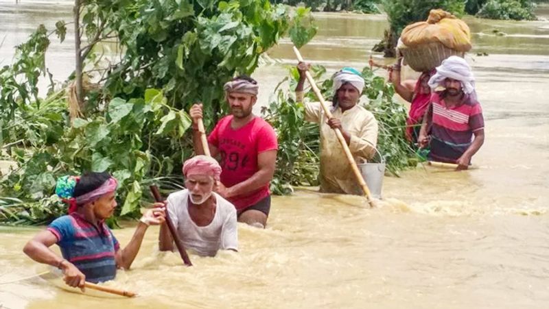 बिहार के मधुबनी जिले में लगातार बारिश के बाद लोग बाढ़ में सड़क पार करते हुए।
