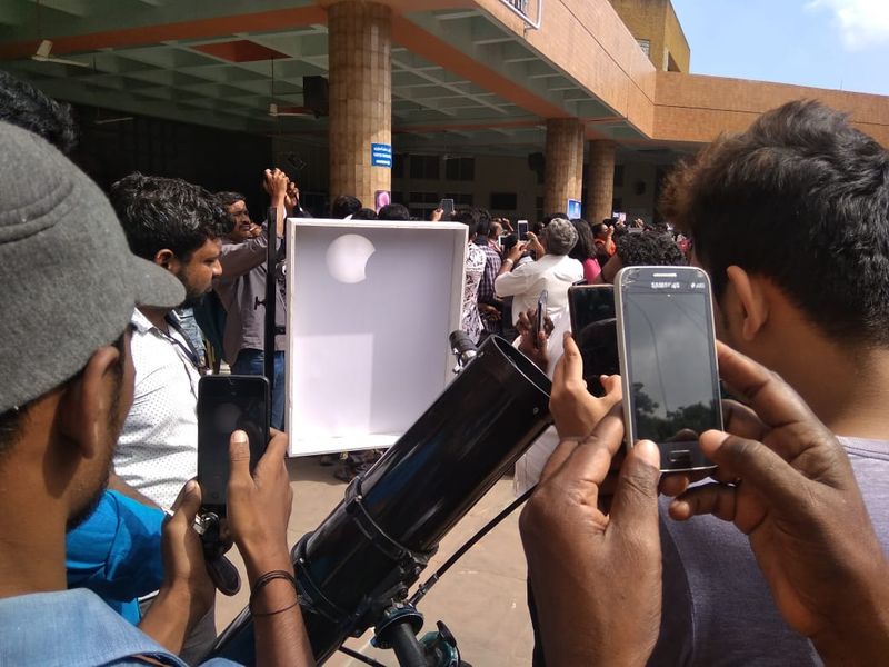 கிரகணத்தின் பிரதிபலிப்பை புகைப்படம் எடுக்கும் சிலர்