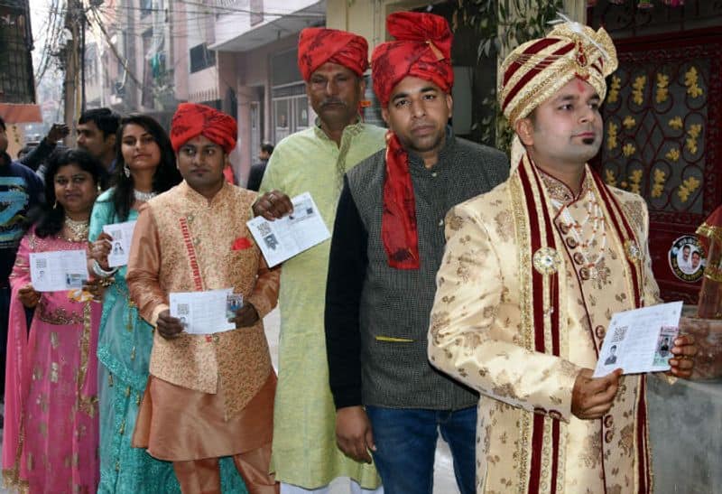 A groom and his family members stand in a queue to cast their vote during the Delhi Assembly election, in New Delhi on Saturday.