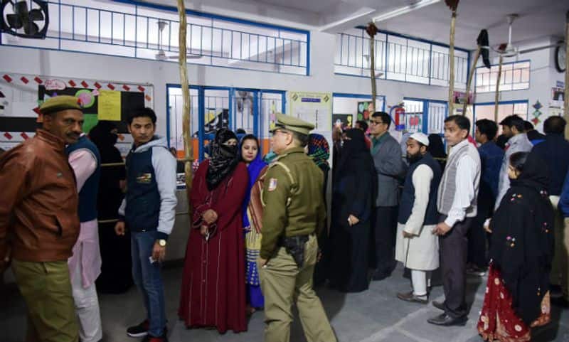 Voters stand in a queue to cast their votes as security personnel stand guard at a polling booth during the Delhi Legislative Assembly elections, at Shaheen Bagh, in New Delhi on February 8, 2020.