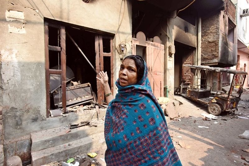 हिंसा के बाद घर में की गई तोड़फोड़ को दिखाती हुई महिला।