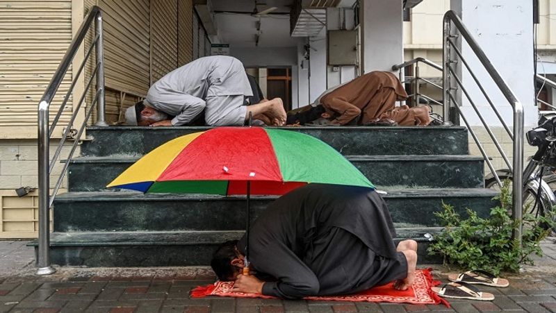 इस्लामाबाद में एक मस्जिद के बाहर नमाज अदा करते लोग। एक शख्स ने धूप से बचने के लिए रंगीन छाता लगा रखा है। 