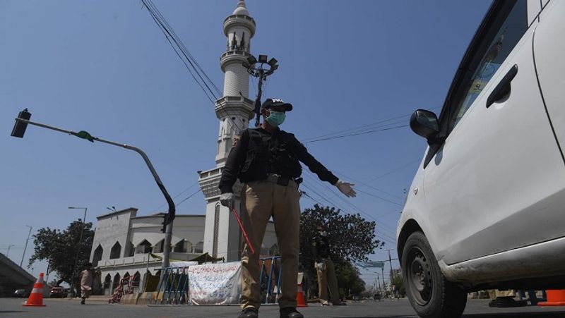 कराची में एक मस्जिद के सामने मास्क पहना पुलिसकर्मी एक कार को आगे बढ़ने से रोक रहा है। 