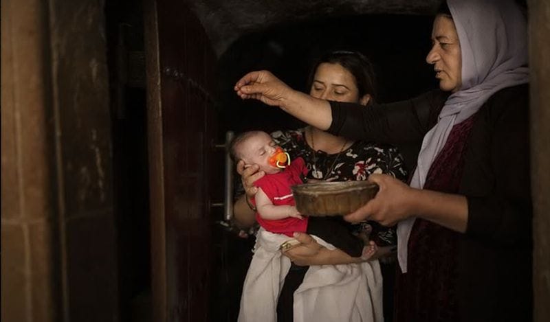 इराक के शेखान के पास लालिश मंदिर में एक यजीदी पवित्र महिला द्वारा एक प्राचीन झरने के पानी से एक बच्ची का अभिषेक करते हुए। 