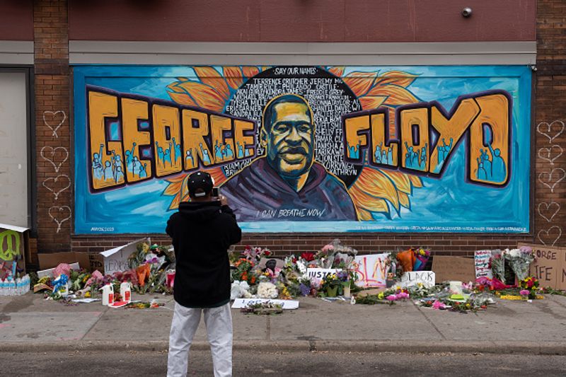 Ronald Scott, a central neighborhood resident for more than 10 years, takes a photo of the memorial mural over flowers and banners laid in the memory of George Floyd outside of Cup Foods on May 29, 2020, in Minnesota, Minneapolis.