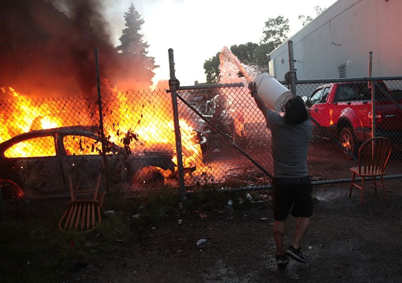 A man attempts to throw water on a car that was set on fire during a protest sparked by the death of George Floyd while he was in police custody on May 29 in Minneapolis, Minnesota.