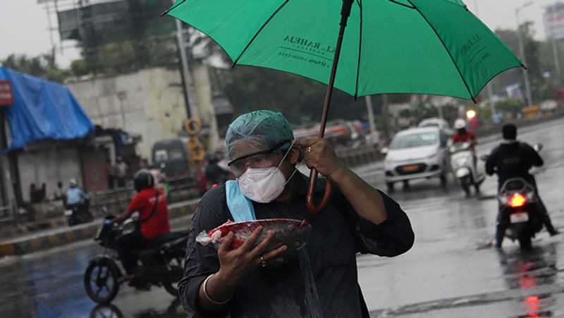 बारिश के बीच घर के लिए खाने-पीने की चीजें लेकर जाती महिला। 