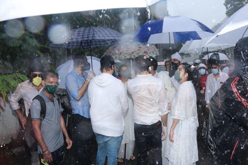 பலர் குடை பிடித்து அஞ்சலி செலுத்த வரிசையில் காத்திருக்கிறார்கள்.