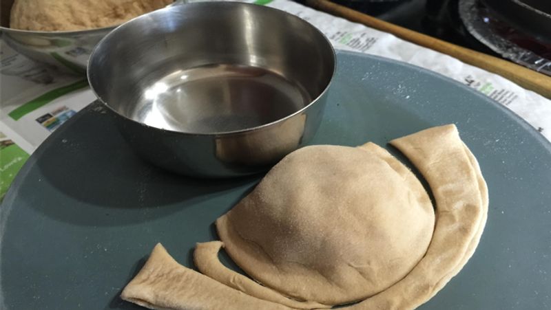 अब एक तेज किनारे वाली कटोरी या चाकू से एक्स्ट्रा आटा निकालें। इसे बराबर करने के लिए इसे धीरे से दबाएं और हल्के हाथ से इसे बेल लें।