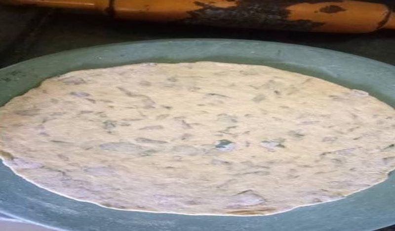 अब गैस पर तवा चढ़ाएं। इसमें आटे से लोई लेकर गोल पराठा बेल डाल दें। 