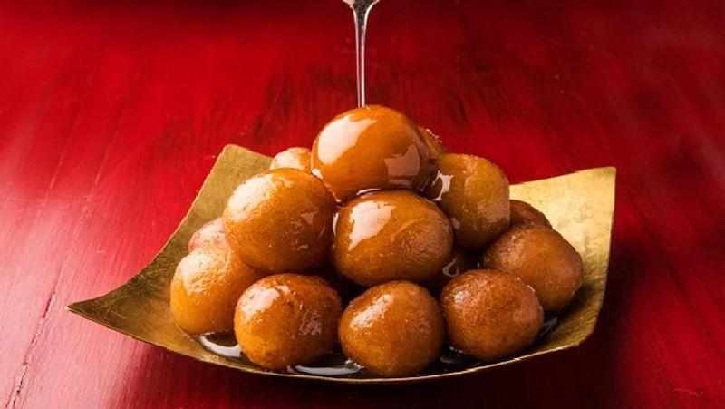 गुलाब जामुन
मीठे का नाम सुनकर किसके मुंह में पानी नहीं आता? और जब बात गुलाब जामुन (Gulab Jamun) की हो, तो क्या कहना। गुलाब जामुन वास्तव में एक भूमध्य व्यंजन है जो गलती से शाहजहाँ के बावर्ची ने बनाया था। हालांकि गुलाब जामुन नाम एक फारसी नाम है, यह मिठाई पहली बार भूमध्यसागरीय क्षेत्र में तैयार की गई थी। जो भी हो हम इस मिठाई के बिना भारत में कोई त्योहार, शादी या पार्टी पूरी नहीं होती।