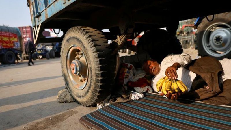 प्रदर्शन स्थल पर ट्राली के नीचे आराम करता किसान। 
