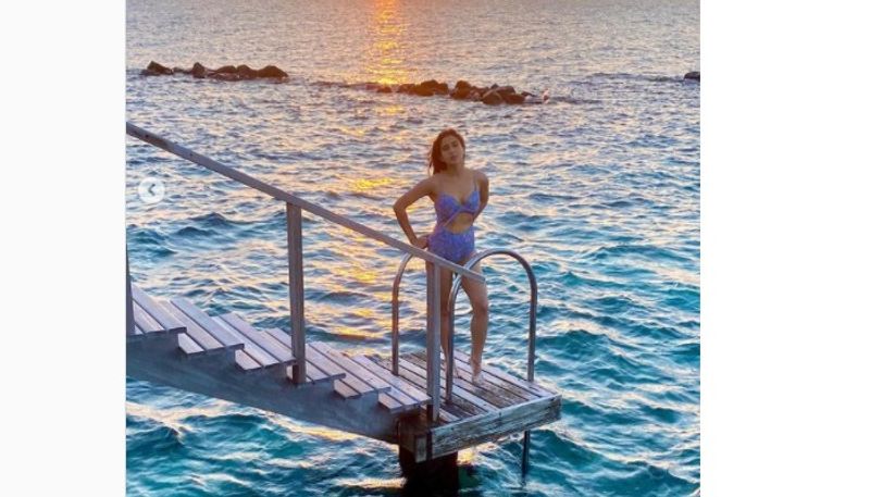Latest, Sara posted a few pictures where she is donning a blue swimsuit, posing in the sun and against the bright blue ocean. She is seen leaning against a large wooden pillar, wearing red sunglasses. 