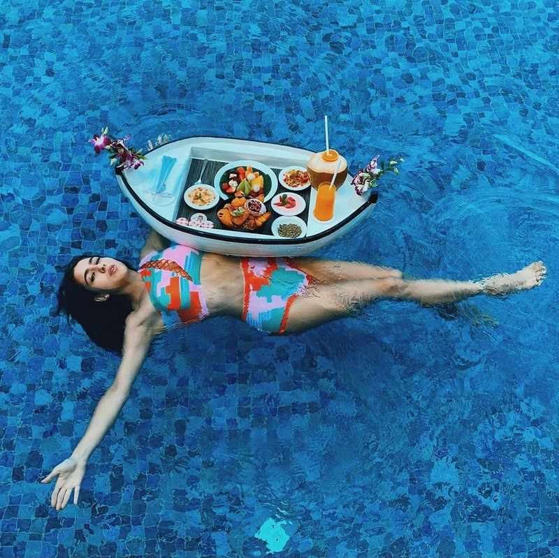 She posed by lying down in between the beach-sky and a boatful of food. She wore a geometry printed blue-orange-pink two-piece swimsuit.