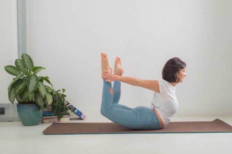 Dhanurasana (Bow pose)
This posture is best for spinal bending and regaining strength. Lie down on your stomach, fold your legs from your knee and bring them to your hips. Touch your ankle with your hands and lift up your head upwards.