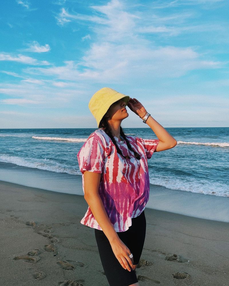 Natasa is seen wearing a striped white-pink top with black half trousers. She dons a hat as she gazes into the sky.