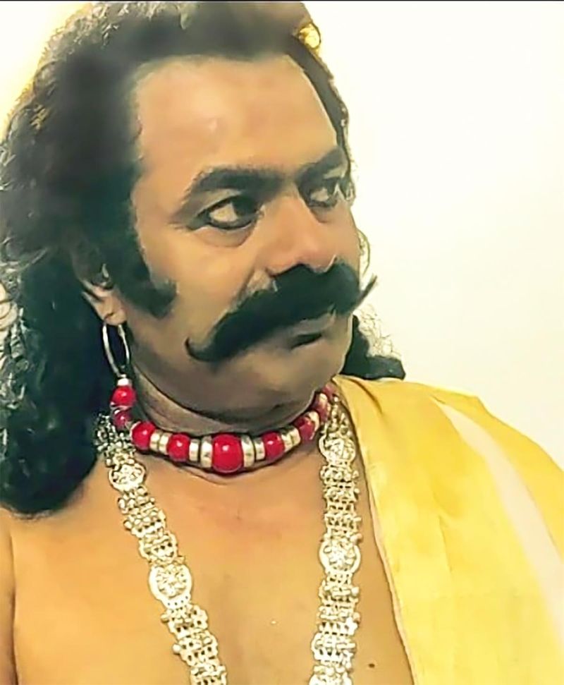 இந்த புகைப்படத்தில்... பெரிய மீசை, கூர்ந்து நோக்கும் கண்கள், நீளமான முடியுடன் உள்ளார்.
