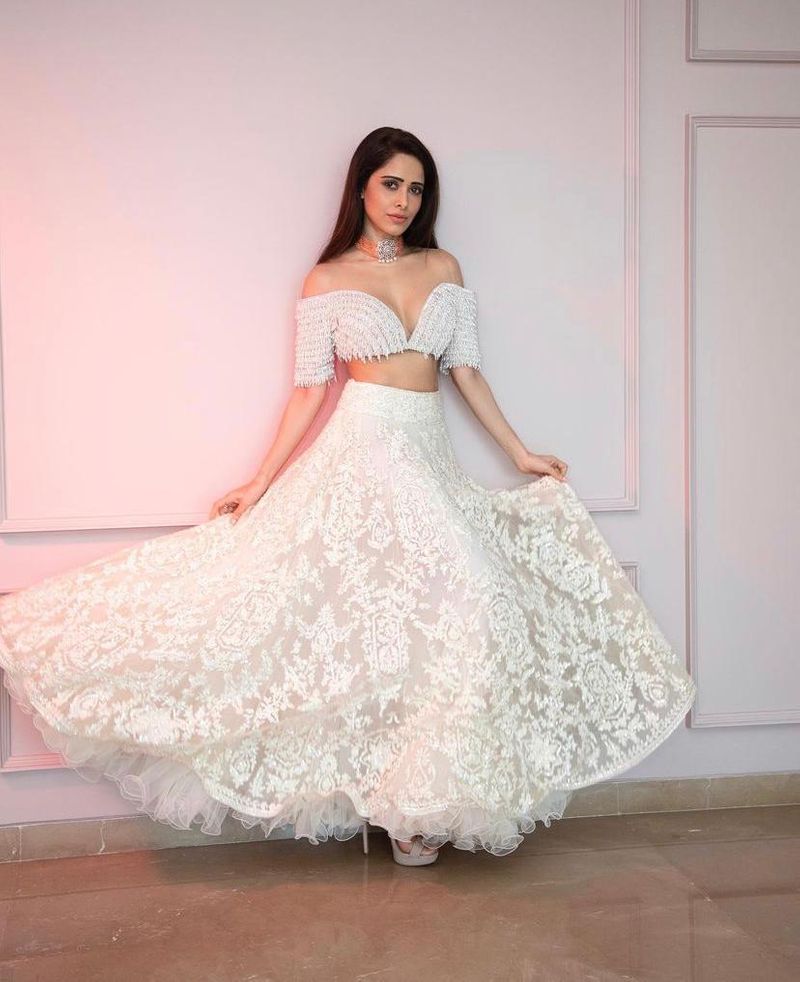 Ethnic Drama
Nushrratt is looking like a vision in this dreamy white lehenga, paired with an off-shoulder blouse. This pristine look is our favourite and made her look nothing less than a princess. Her makeup is kept at a minimum, combined with a diamond choker.