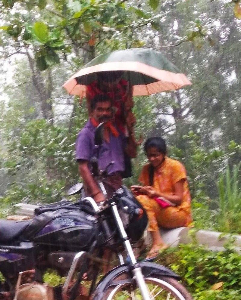 father holds umbrella to daughter  as she attends online class by the road
