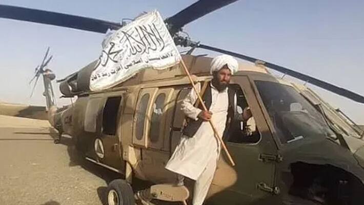 Taliban brutality in Afghanistan Gunman patrolling in Black hawk chopper with hanging a man from it Taliban brutality in Afghanistan Gunman patrolling in Black hawk chopper with hanging a man from it