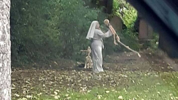 woman dressed as nun dances with dog and human sketeton next to graveyard pod woman dressed as nun dances with dog and human sketeton next to graveyard pod
